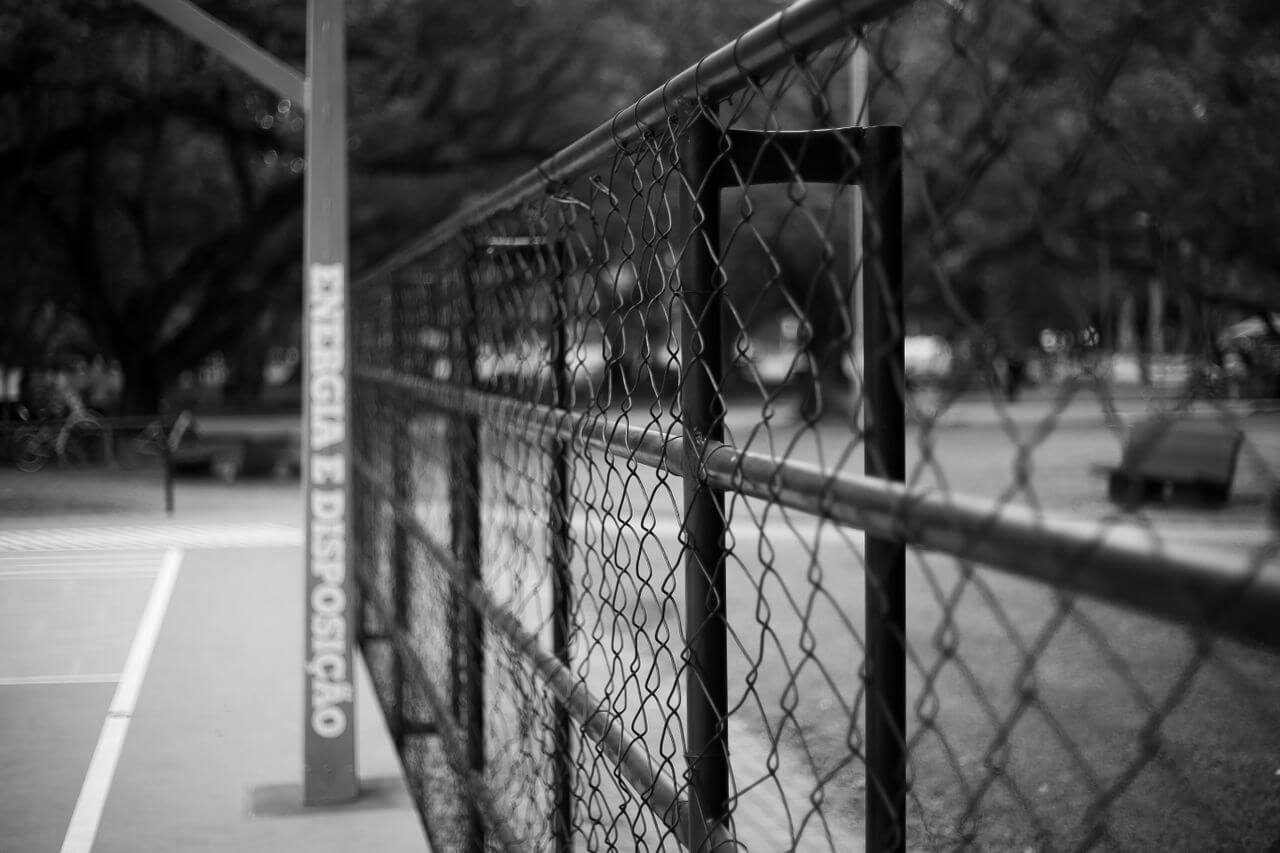 Black and white image of a chain link fence in an outdoor park.